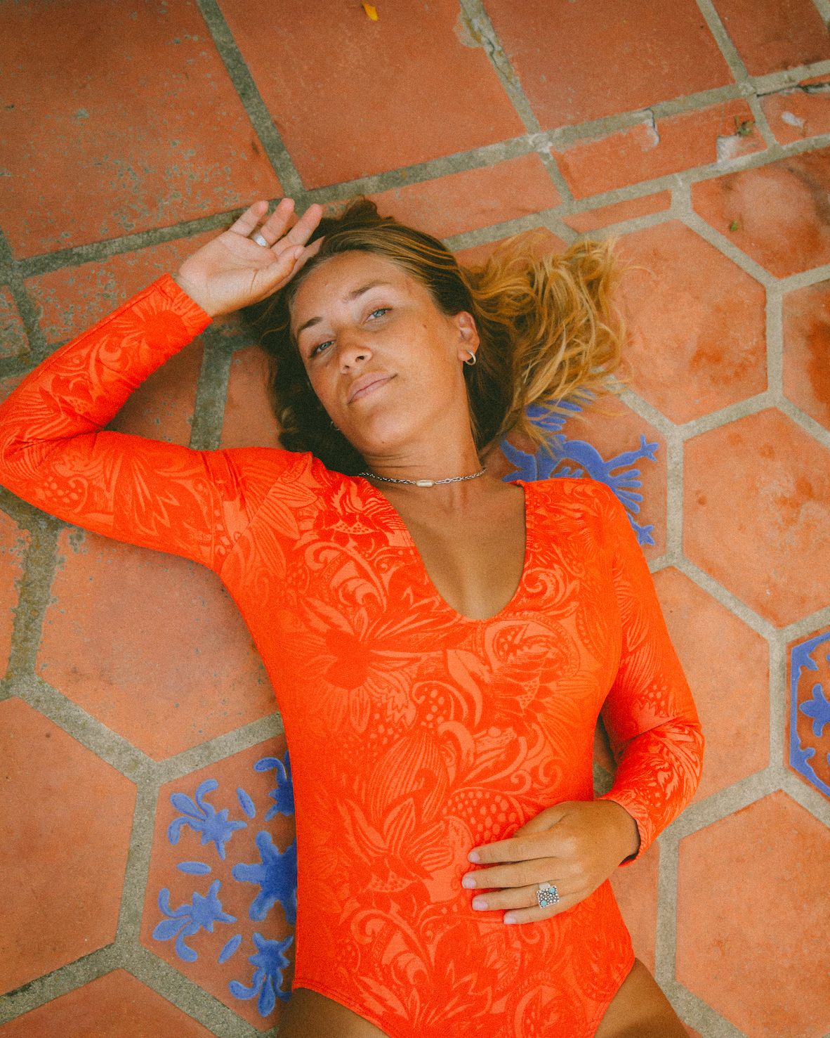 Woman in an orange patterned swimsuit lying on a terracotta-tiled floor.